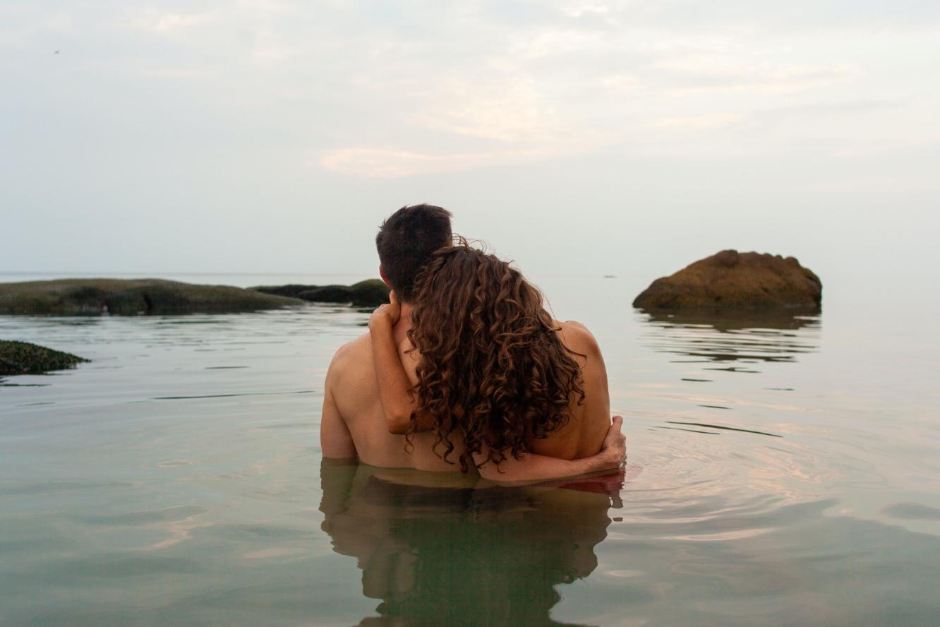 Pareja heterosexual desnudos en el océano abrazados viendo al horizonte